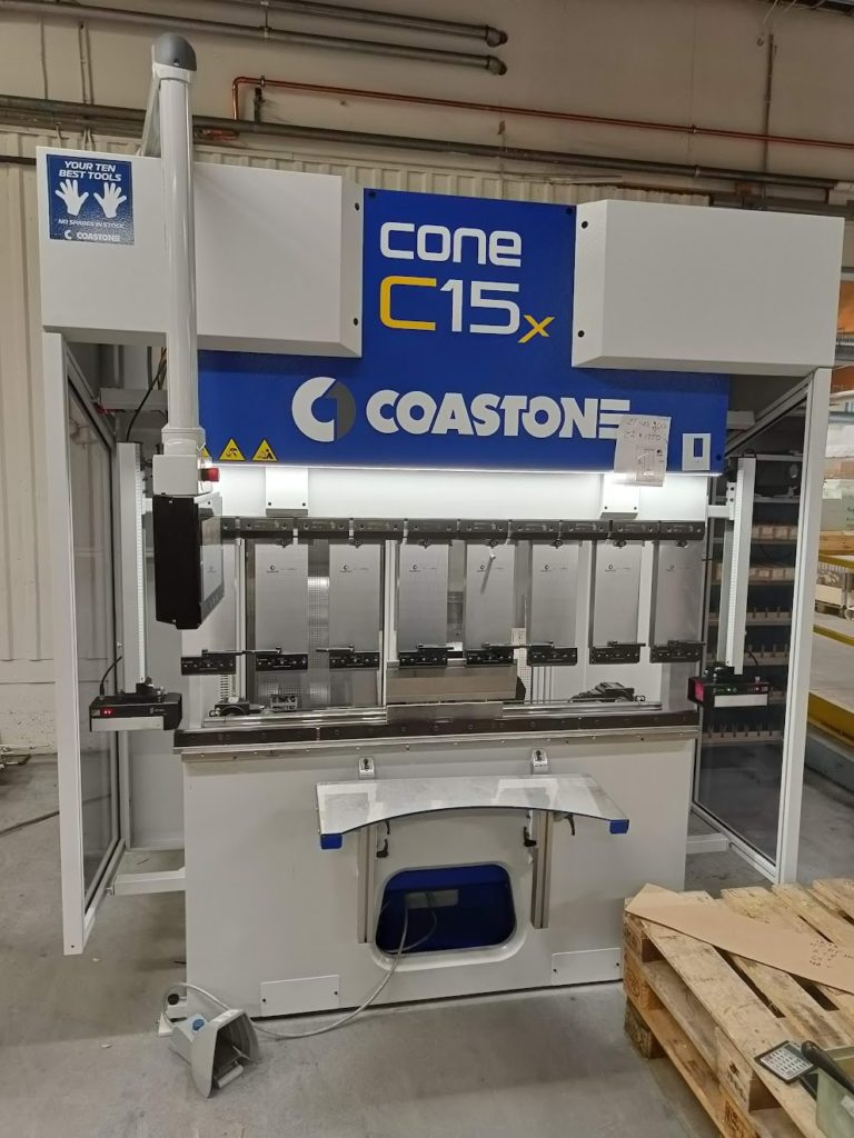 Särmäys eli ohutlevyosien taivutuskone seisoo tehtaalla, ja se on varustettu ohjauspaneeleilla ja näkyvillä turvamerkinnöillä. Puinen kuormalava lepää läheisellä betonilattialla.